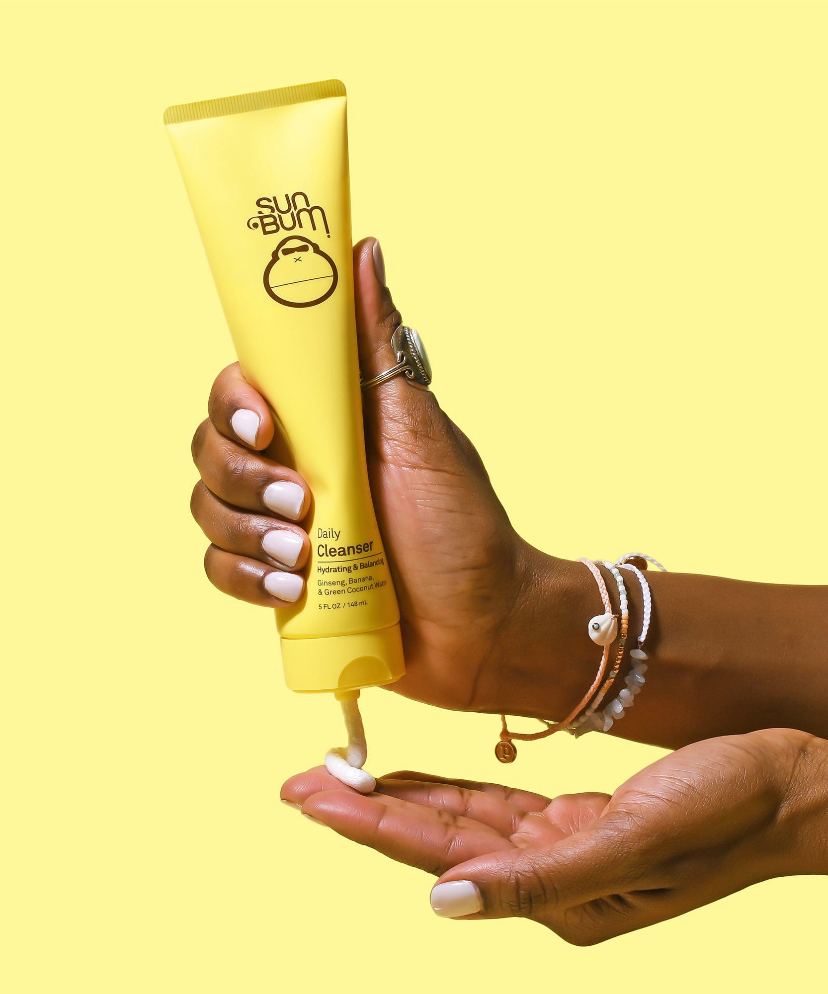 Hand holding Sun Bum Daily Cleanser tube, dispensing product onto palm with yellow background. Sun Bum.