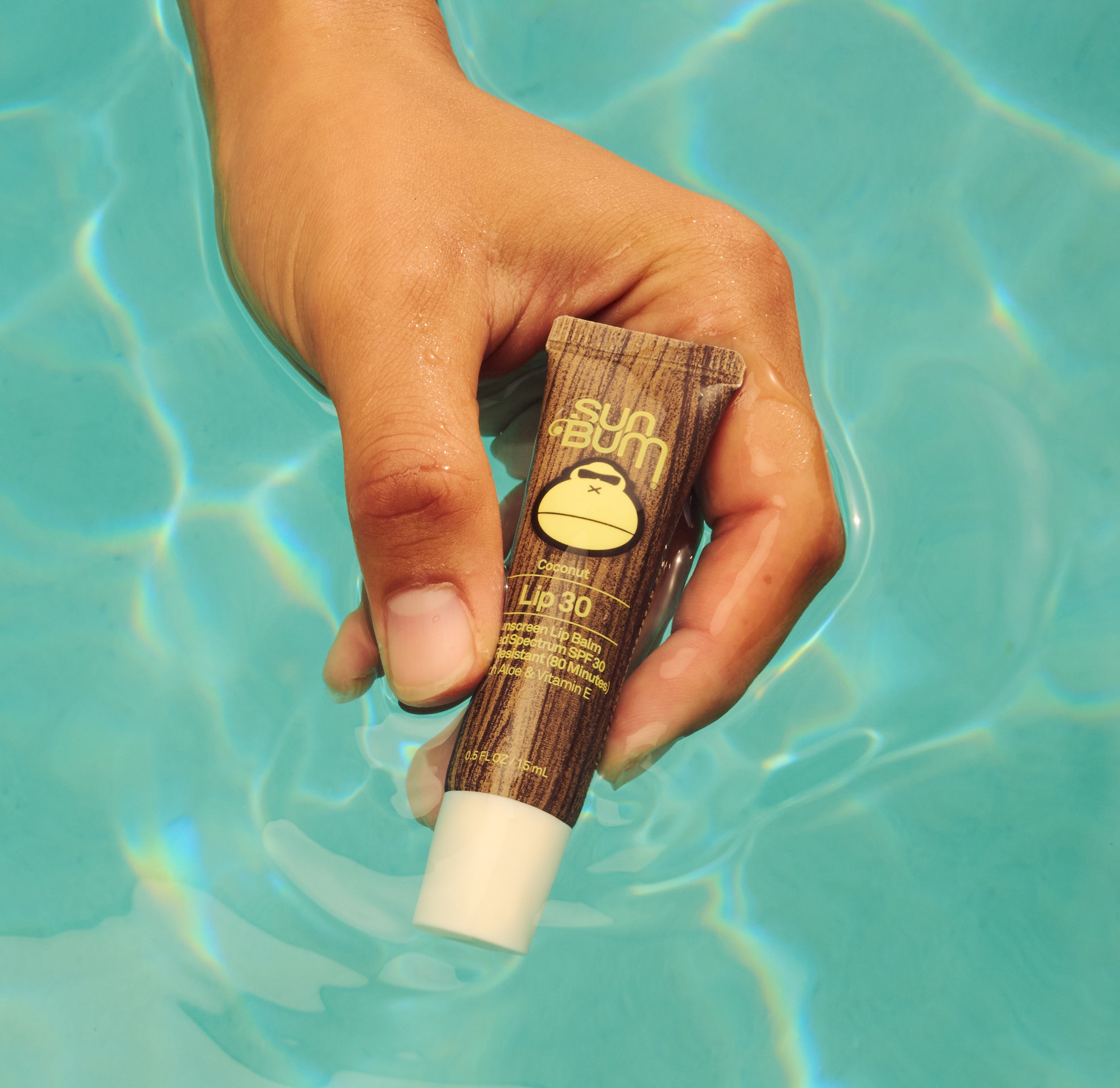 Hand holding Sun Bum Lip 30 in the pool
