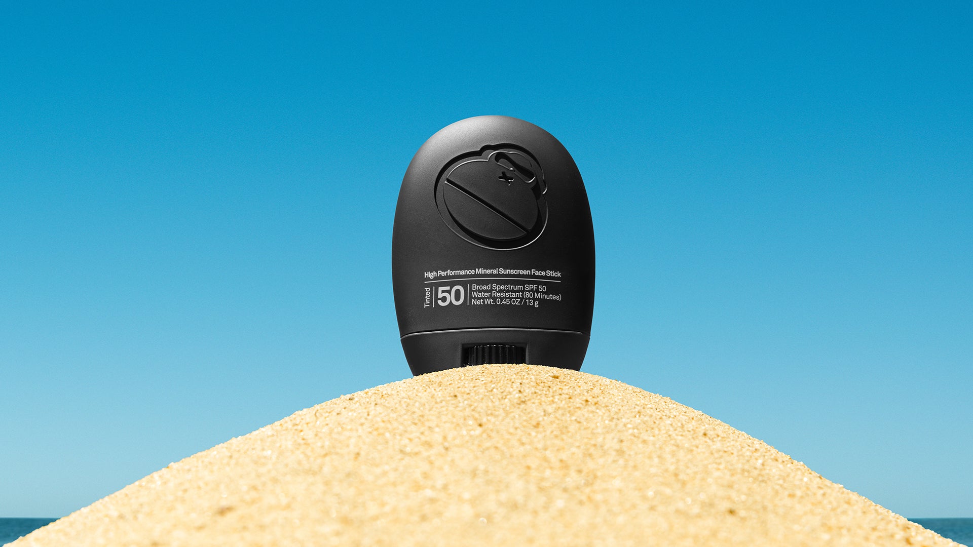 Signature Face Stick on top of a sand hill with a blue background.