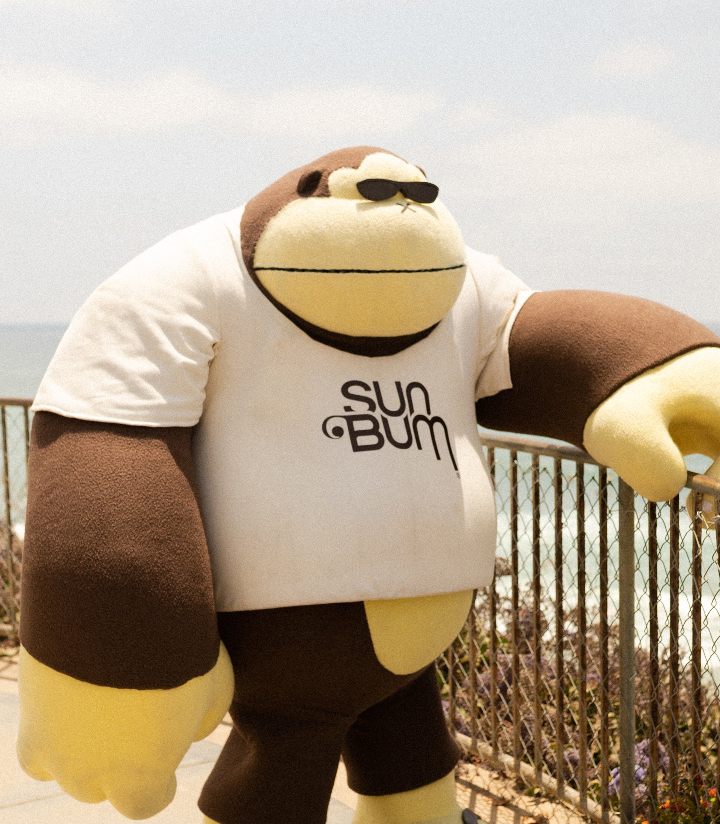 Sonny mascot chillin' oceanside in shades and Sun Bum tee, radiating laid-back beach vibes - Ask The Bum Collection - Sun Bum