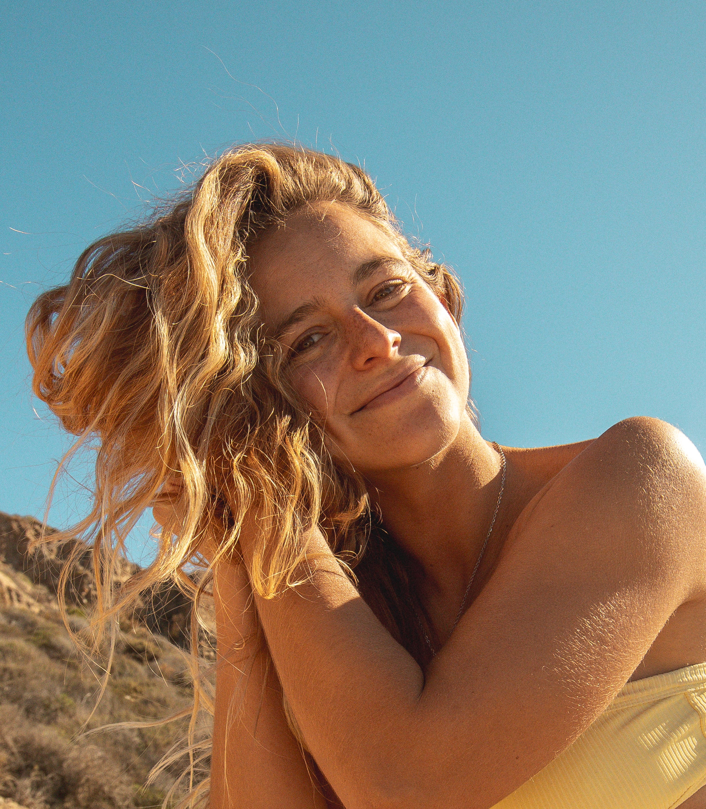 Smiling woman with sun-kissed blonde waves outdoors, highlighting the SB Blonde Hair Care Collection – Sun Bum.
