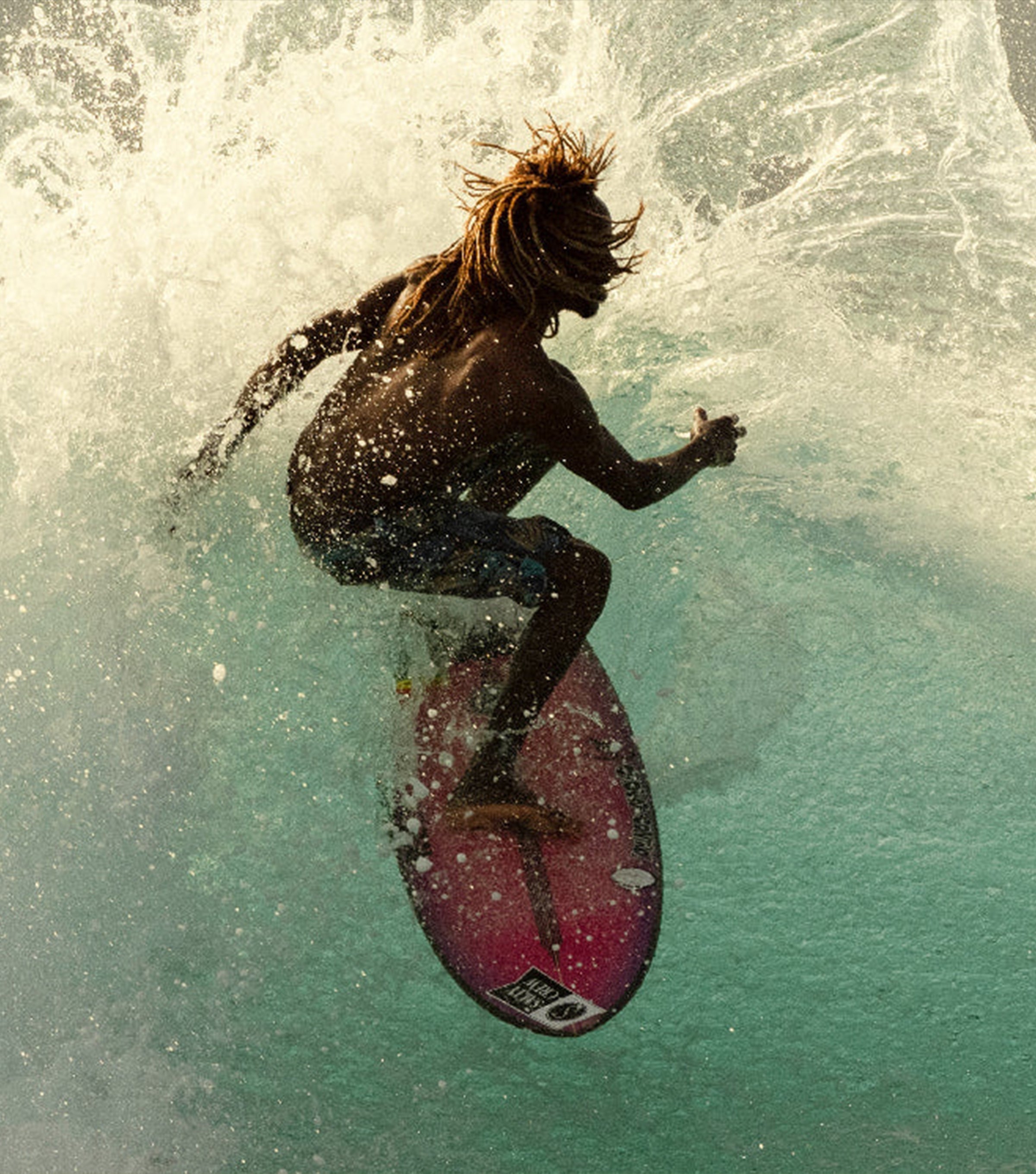 Surfer catching air off a wave at golden hour, showcasing the energy of the Discover Ambassador Collection - Sun Bum.