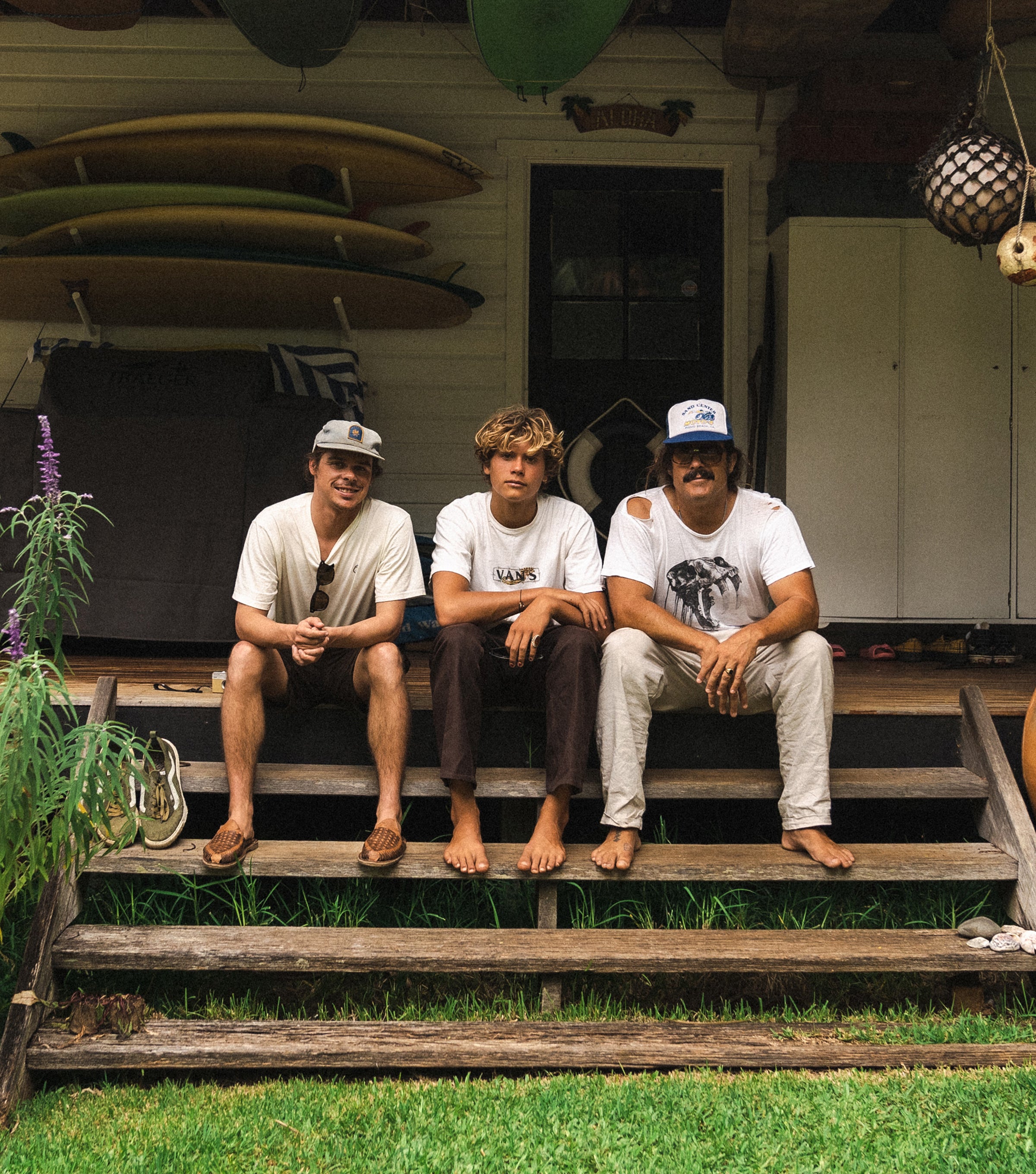 Three friends sitting on a porch surrounded by surfboards and tropical vibes, featured in the Discover Blog Collection - Sun Bum.