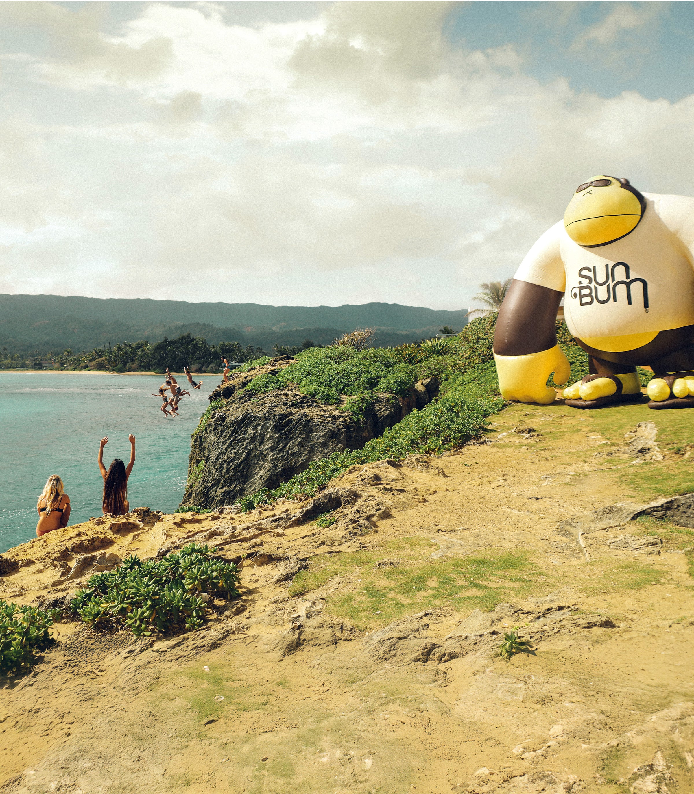 Friends cliff jump into turquoise water beside a giant inflatable gorilla on a sunny coast – Discover Collection - Sun Bum.