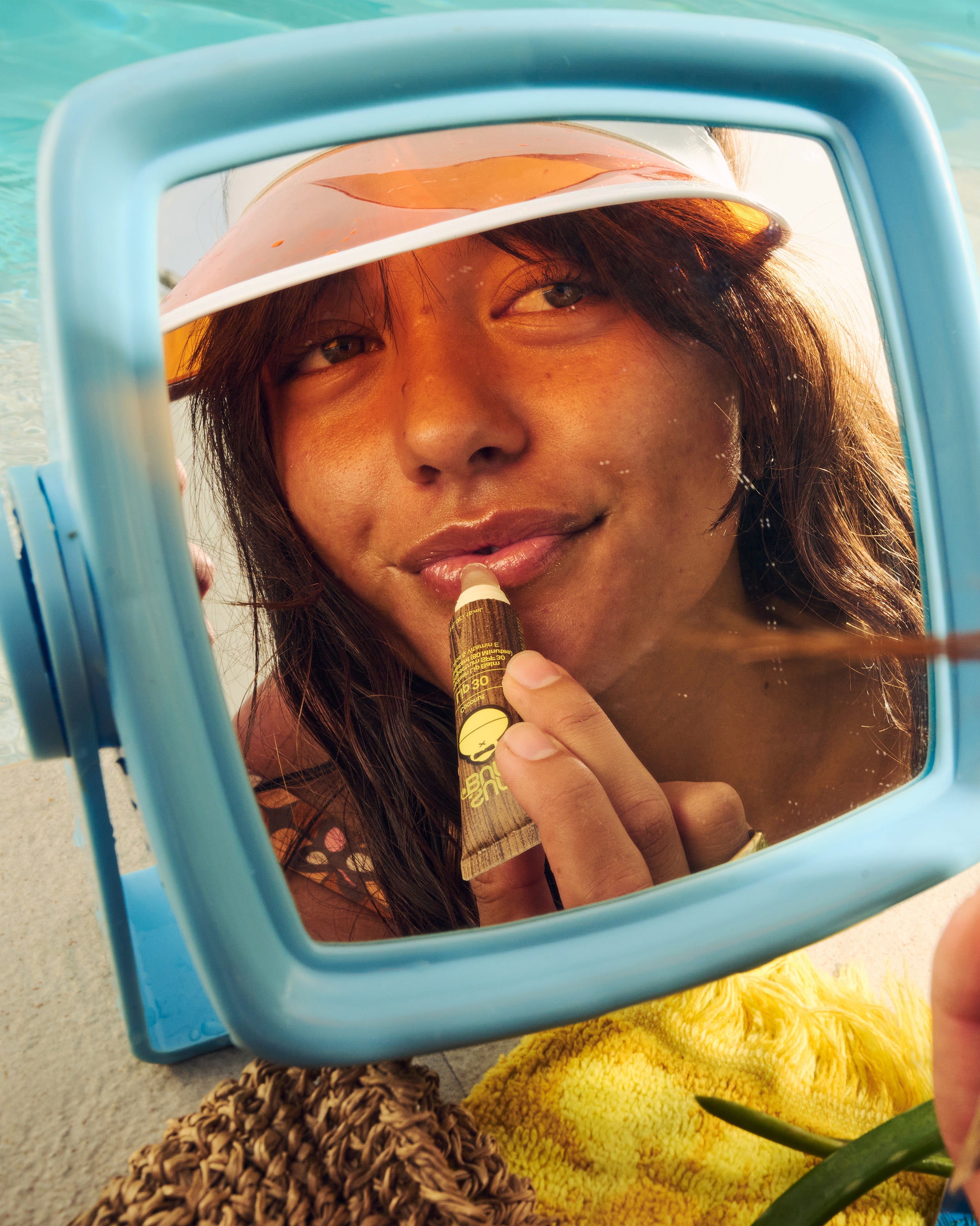 Woman applying Sun Bum's Lip 30 on her lips looking in a mirror