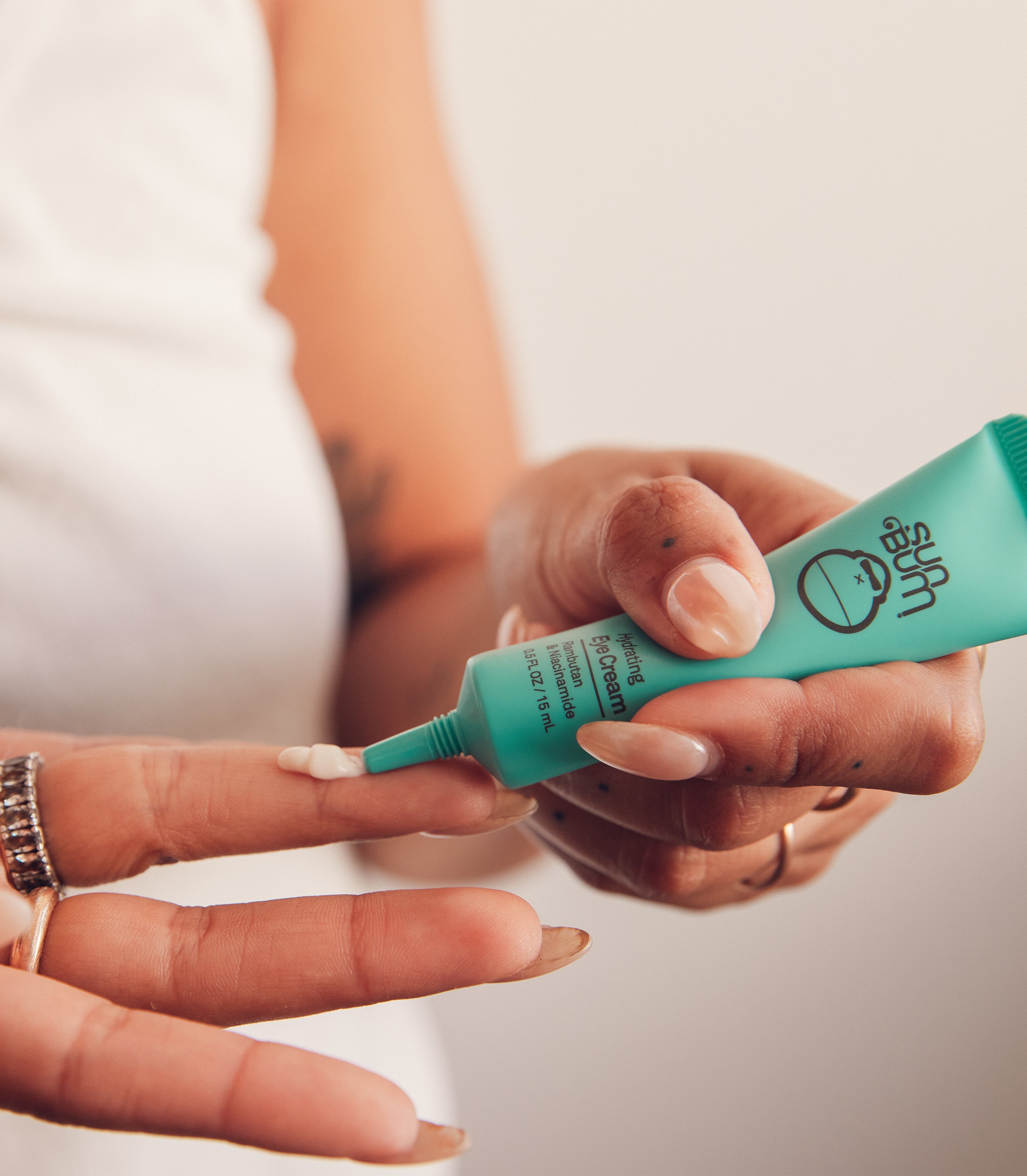 Close-up of hands applying eye cream from a turquoise tube, highlighting the SB Hydrating Skin Care Collection – Sun Bum.