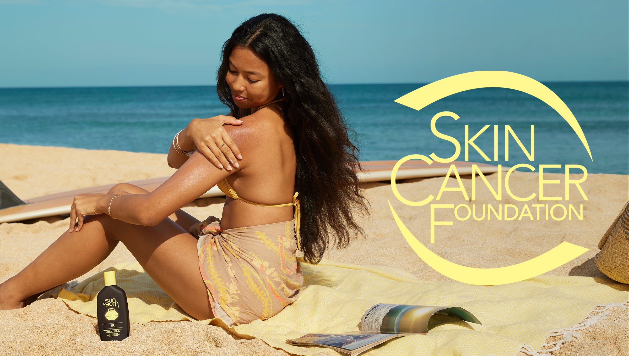 Woman applying sunscreen on the beach next to SPF lotion bottle, highlighting sun safety from the Know Your Spots Collection - Sun Bum.