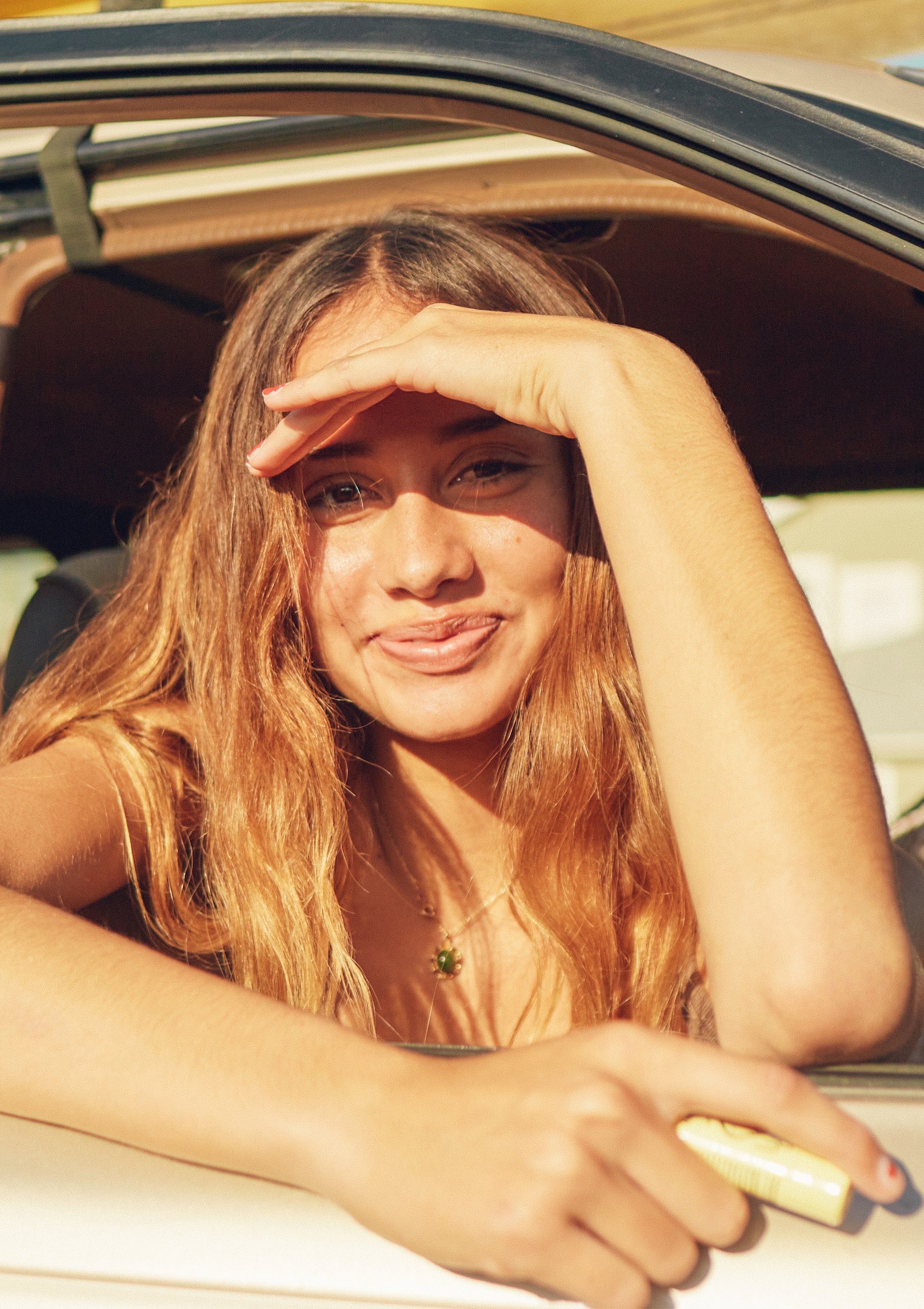 Smiling girl shades her eyes in the sun while holding hydrating lip balm to soothe dry lips – Promo Blocks Lifestyle Lip Collection - Sun Bum.
