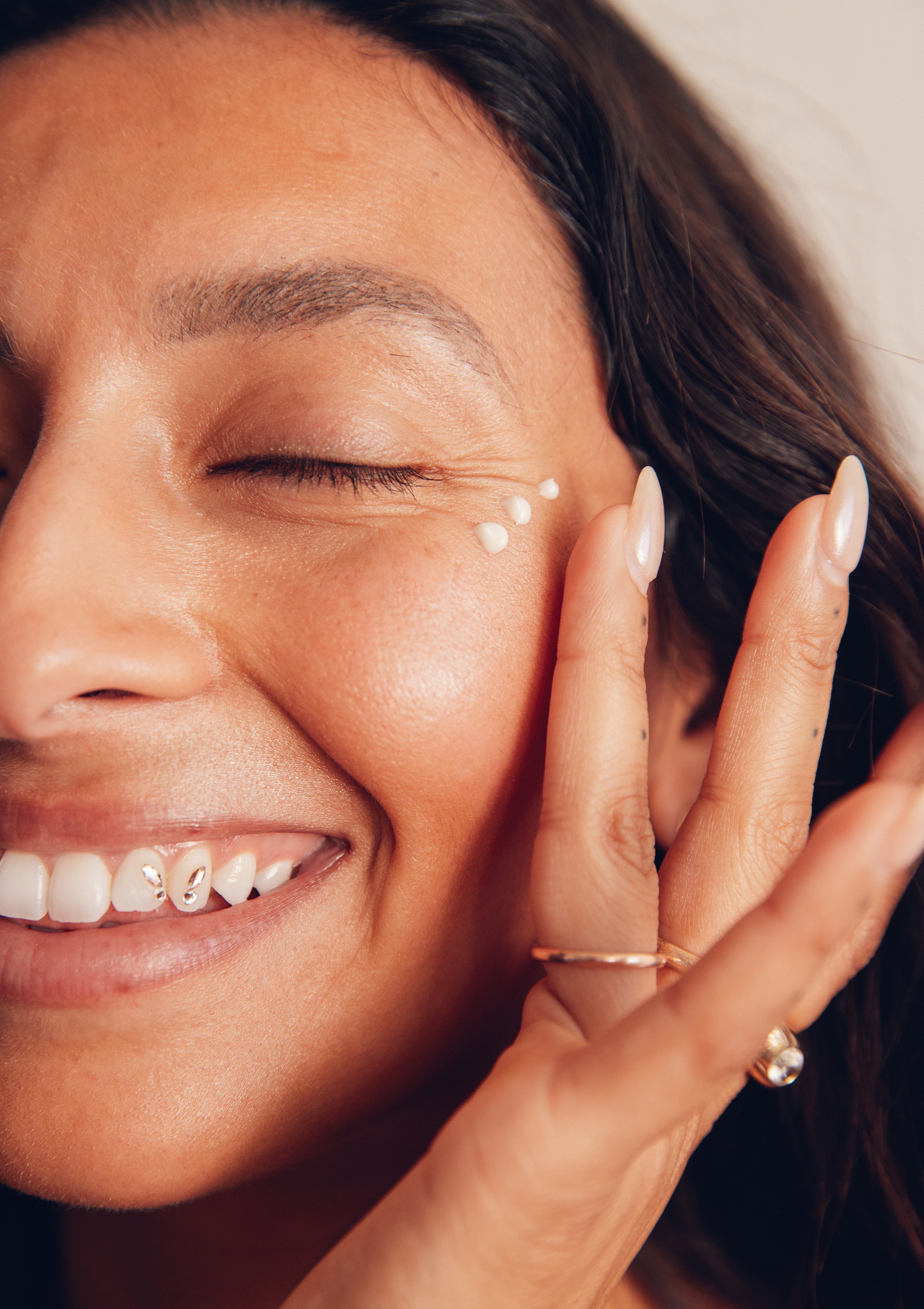 Woman smiling with eyes closed while applying hydrating cream under her eye – Promo Blocks Lifestyle Skin Hydrating Collection - Sun Bum.