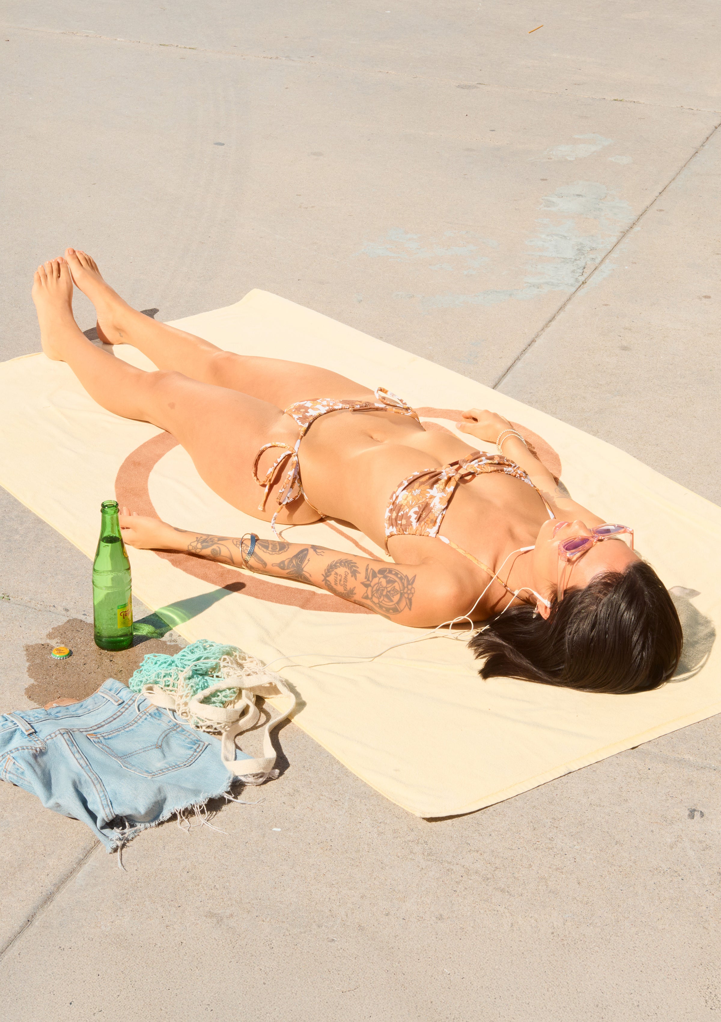 Woman sunbathing in a bikini on a beach towel with summer essentials nearby – Promo Blocks Lifestyle Sun Collection - Sun Bum.