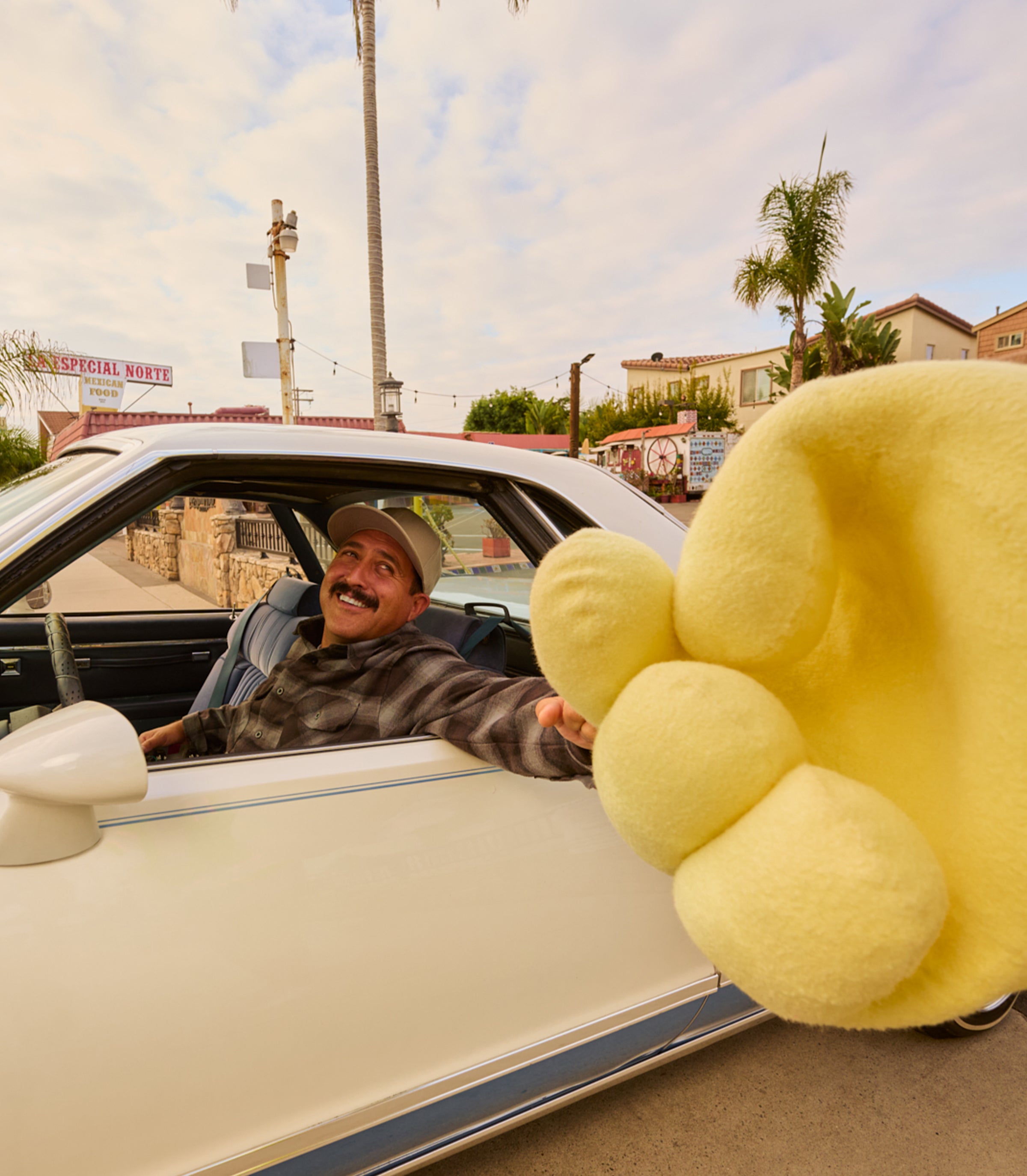 Man smiling from a car window giving a high five to a giant Sonny hand, featuring the SB Shop All Collection – Sun Bum.