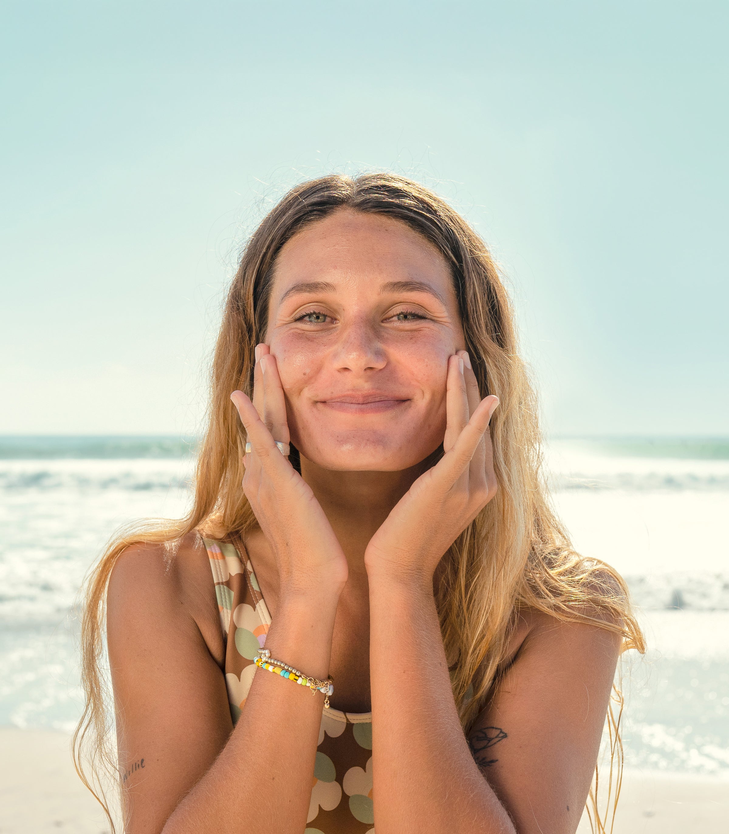 Smiling woman gently applying skincare at the beach, highlighting the SB Skin Care Collection – Sun Bum.