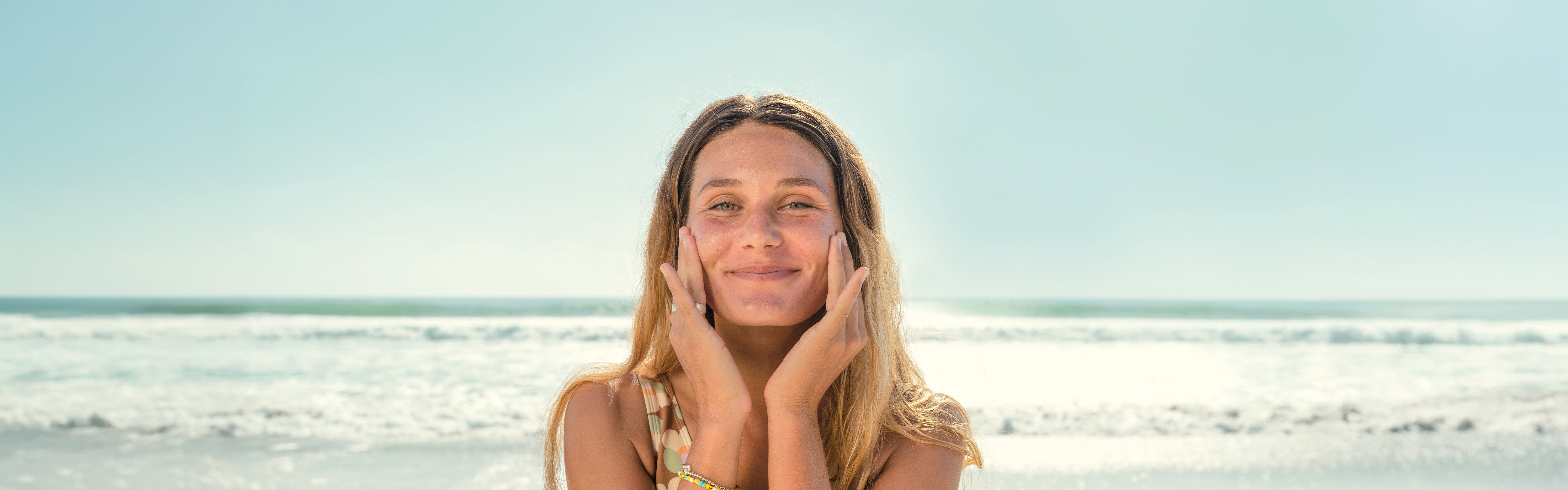 Smiling woman gently applies skincare while enjoying a sunny beach day – Daily Face Collection - Sun Bum.