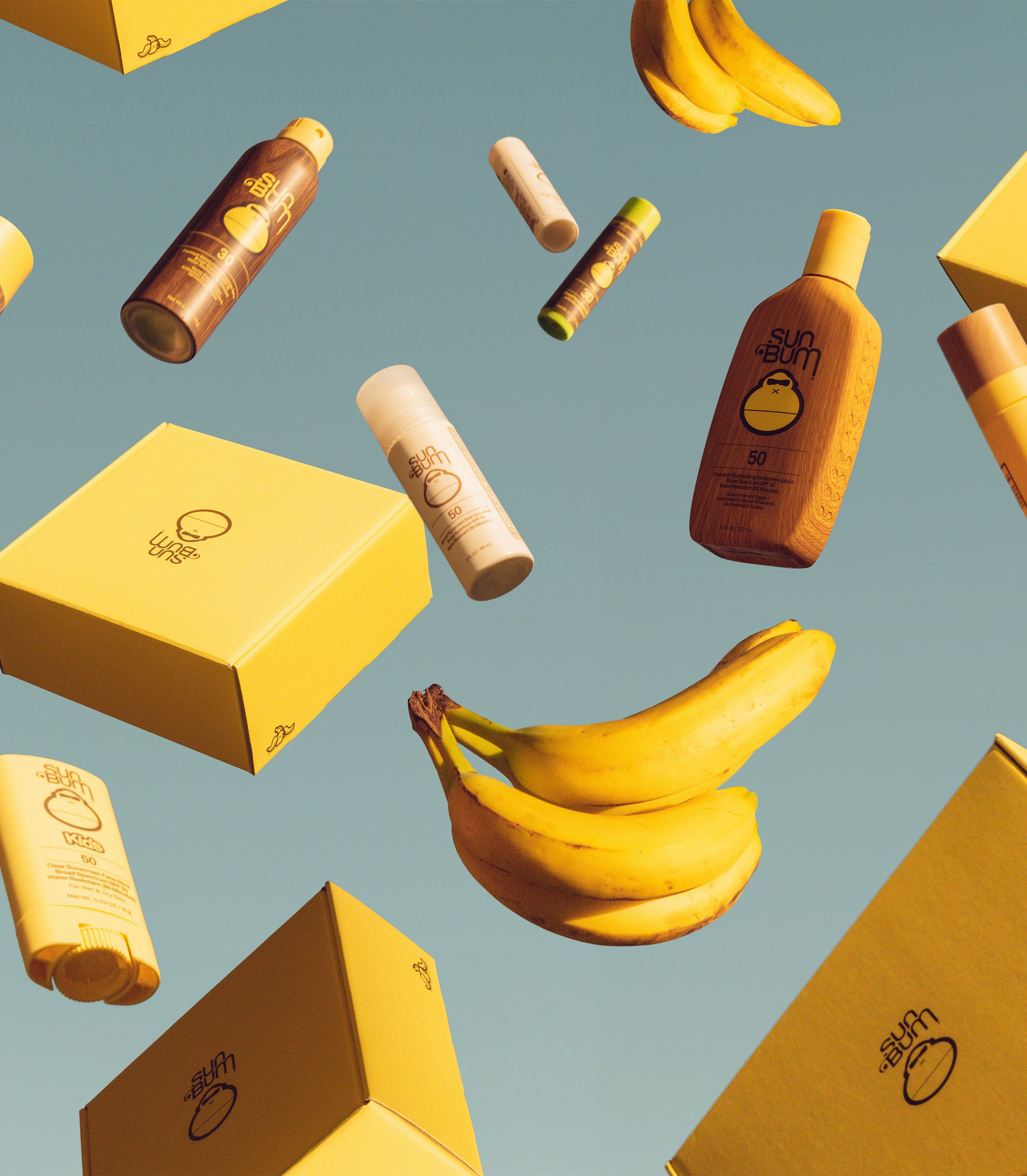 Floating Sun Bum products, boxes, and bananas pop against a blue sky in a playful display – Subscriptions Collection - Sun Bum.