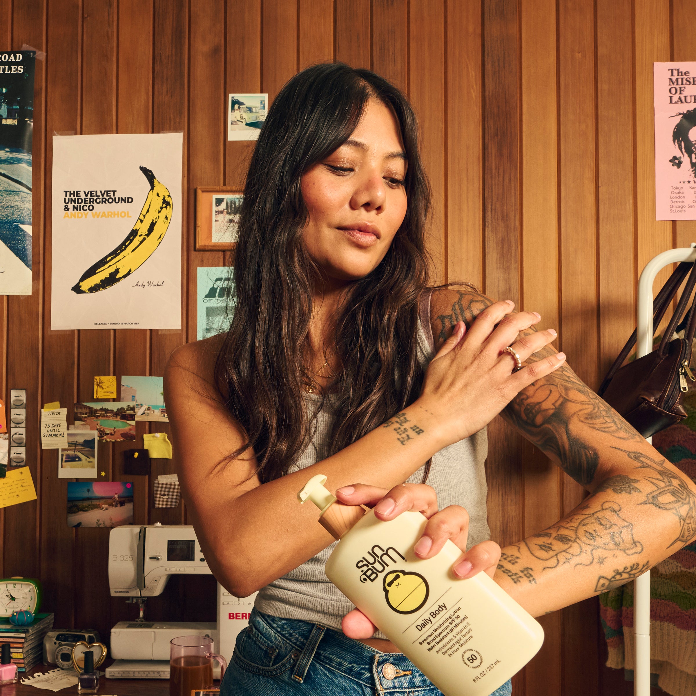 Tattooed woman applying body sunscreen indoors for all-day hydration – Daily Collection - Sun Bum.